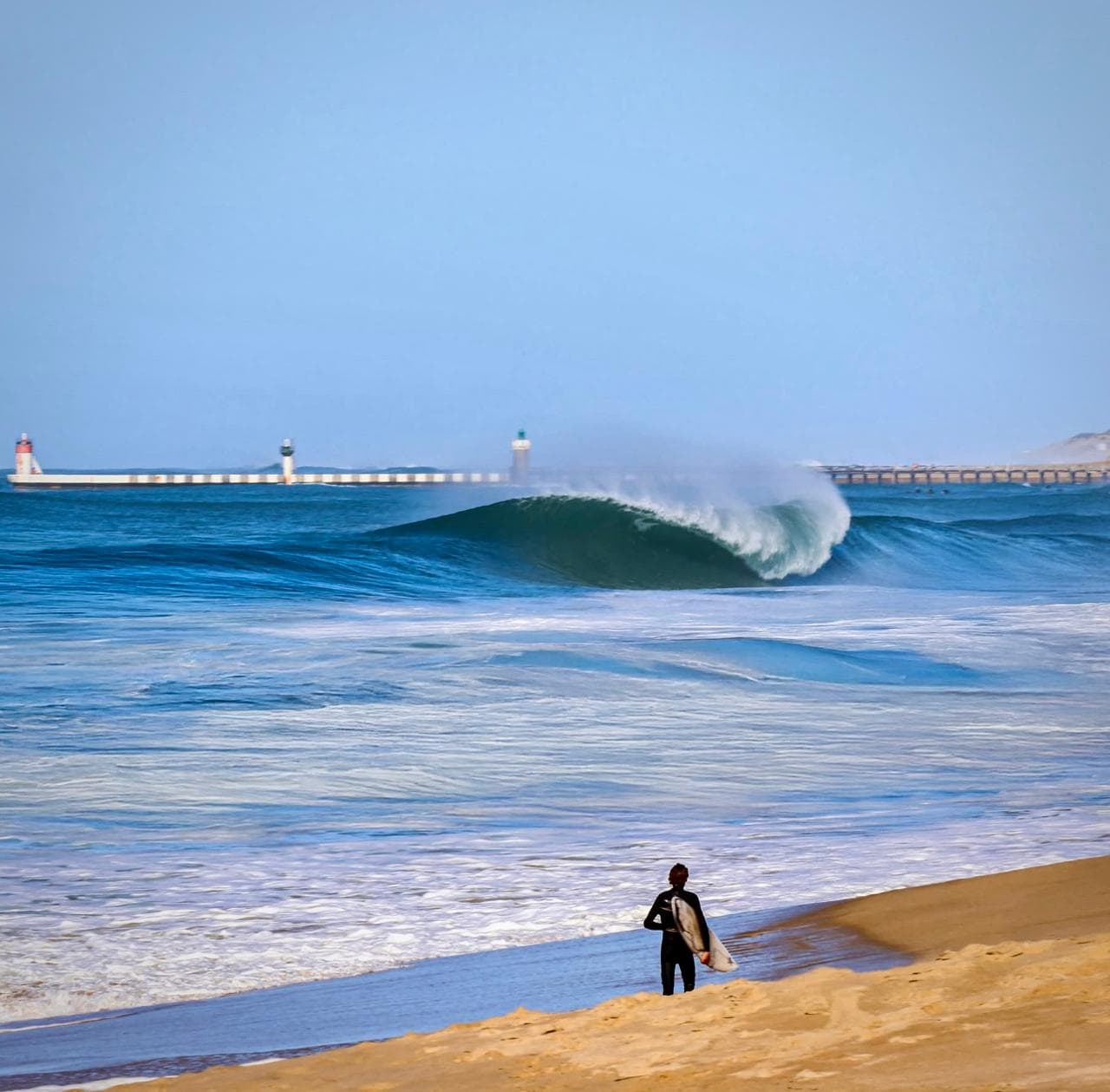 Surfeur sur une vague bleue devant le phare de Capbreton